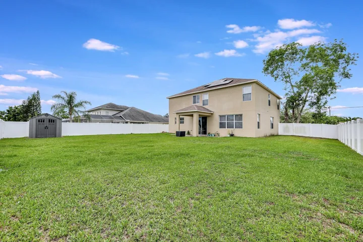Expansive backyard featuring a manicured lawn, a white privacy fence, and a detached storage shed