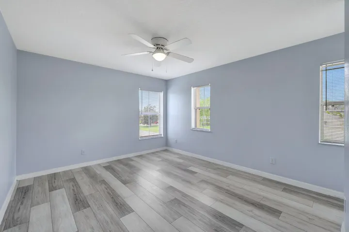 Light-toned wood-finish flooring, multiple windows, ceiling fan with integrated lighting, and neutral wall tones