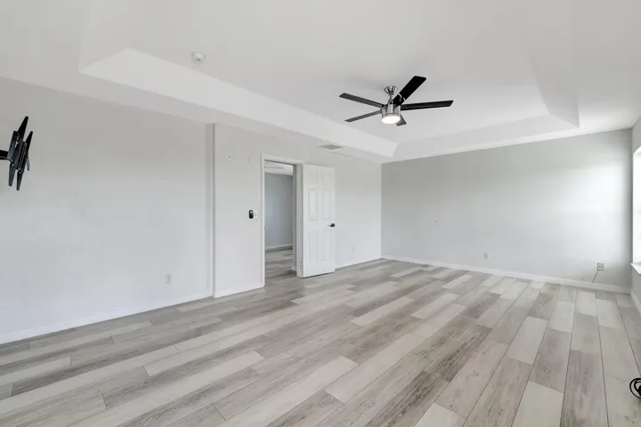 Spacious room featuring wood-finish flooring, a tray ceiling, and a ceiling fan with integrated lighting