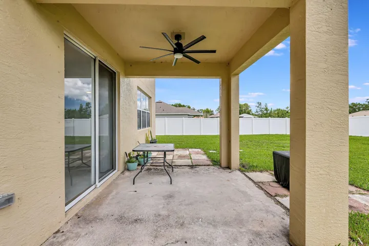Covered patio with a ceiling fan, concrete flooring, and an expansive lawn