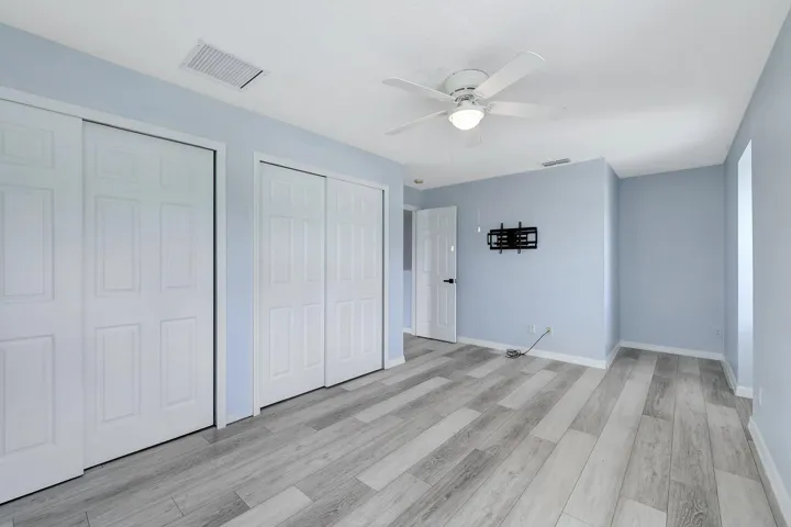 Light blue walls, wood-finish flooring, white panel doors, and a ceiling fan with integrated lighting
