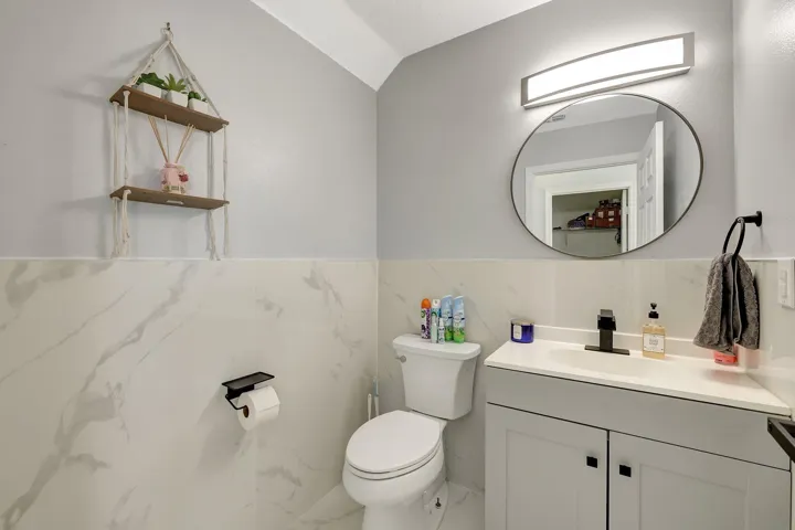 White-and-gray wall tile, white vanity with inset sink, matte black faucet, and oval mirror with wall-mounted lighting