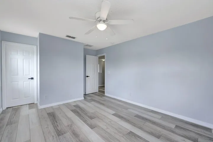 Light wood-finish flooring, white paneled doors with black hardware, recessed wall, and a ceiling fan with integrated lighting