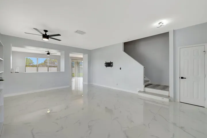 Polished tile flooring, modern ceiling fan, interior staircase with wood-finish treads, built-in shelving, and white panel door with black hardware