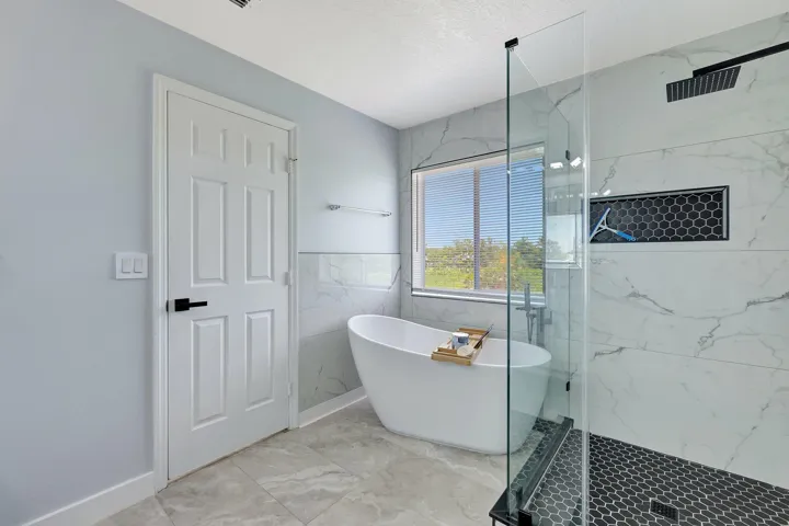 Freestanding bathtub, glass-enclosed shower, rain shower head, hex tile shower floor, and large format tile flooring