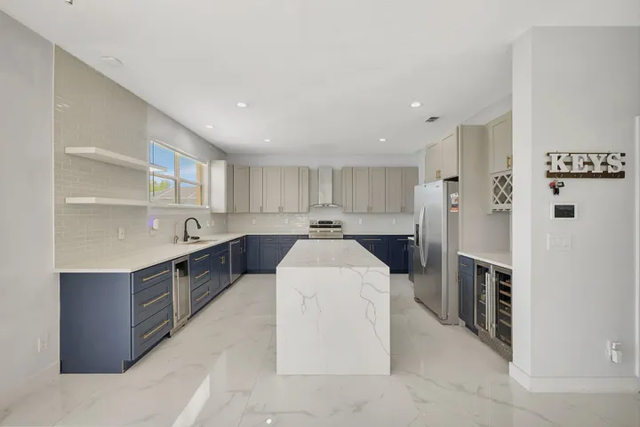 Kitchen featuring a substantial center island with integrated countertop, stainless steel appliances, two-tone cabinetry with gold-tone hardware, and a tile backsplash