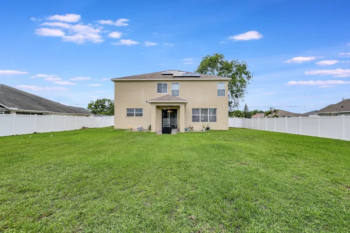 Expansive green space with a full vinyl privacy fence, a stucco exterior, and solar panels
