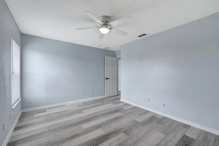 Light-toned wood-finish flooring, ceiling fan with integrated lighting, and a window with blinds