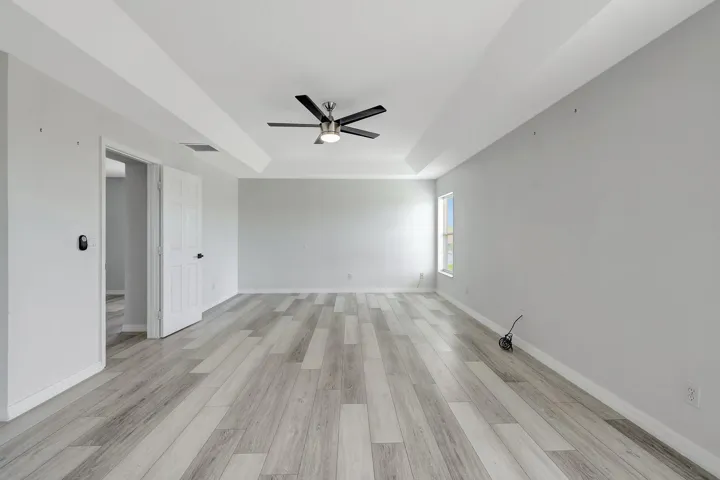 Recessed tray ceiling, contemporary ceiling fan, wood-finish flooring, white paneled doors, and a window providing natural light