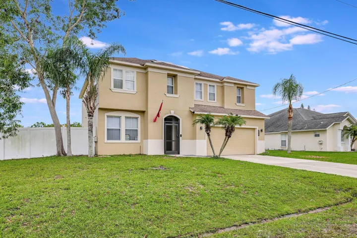 Two-story stucco exterior, attached garage, well-maintained lawn, privacy fencing, and mature palm trees