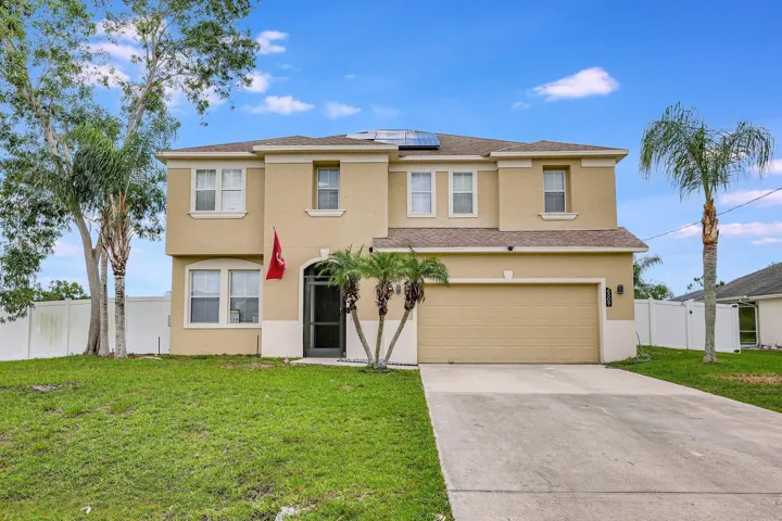 Two-story stucco exterior with an arched entry, attached garage, concrete driveway, and white privacy fencing