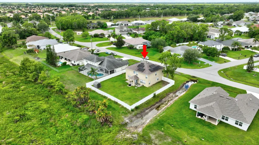 Two-story residence with a pitched roof and multiple solar panels, set on a grassy lot with a white privacy fence