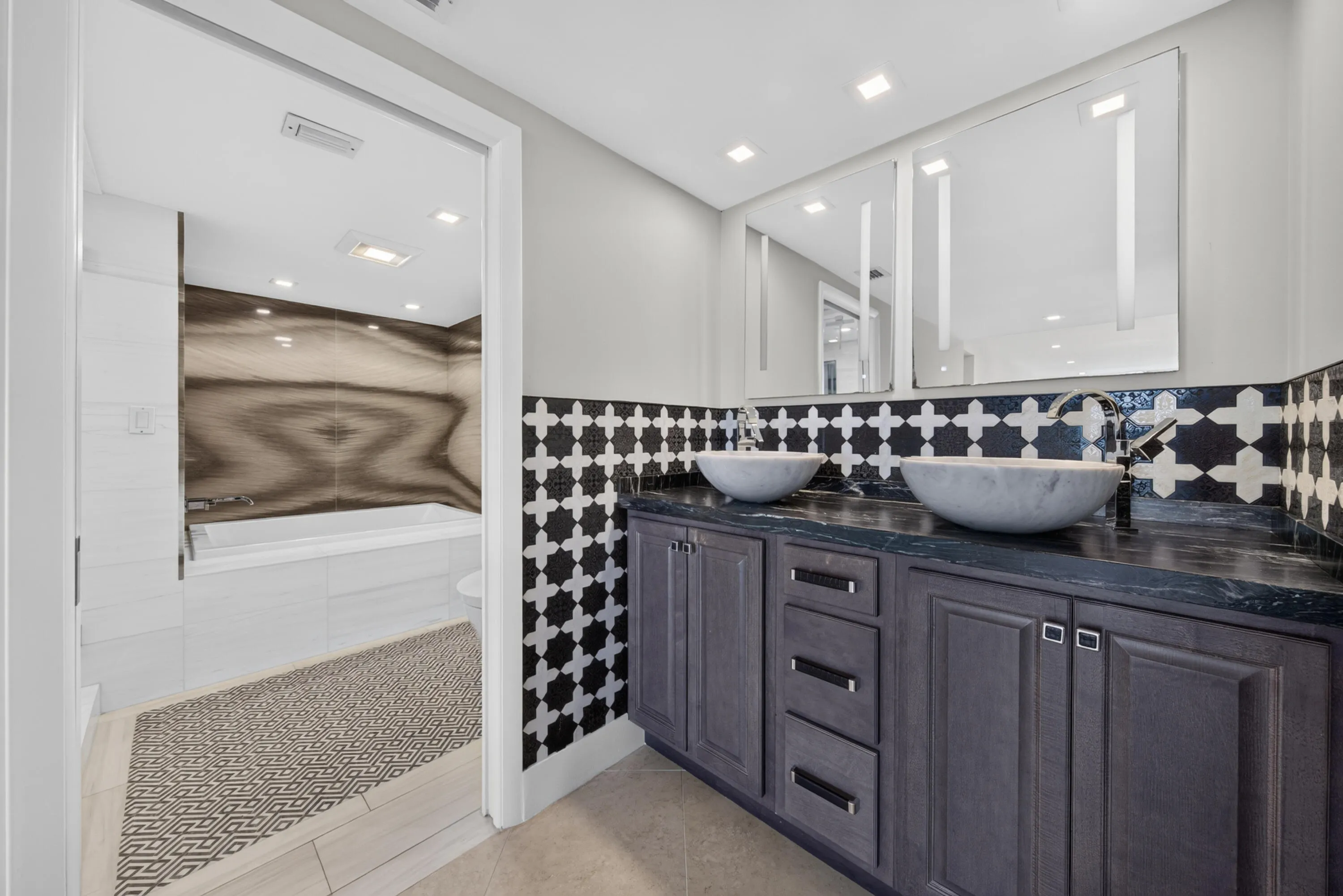 A custom dual vanity, vessel sinks, illuminated mirrors and bold tilework create a distinctive luxury retreat.