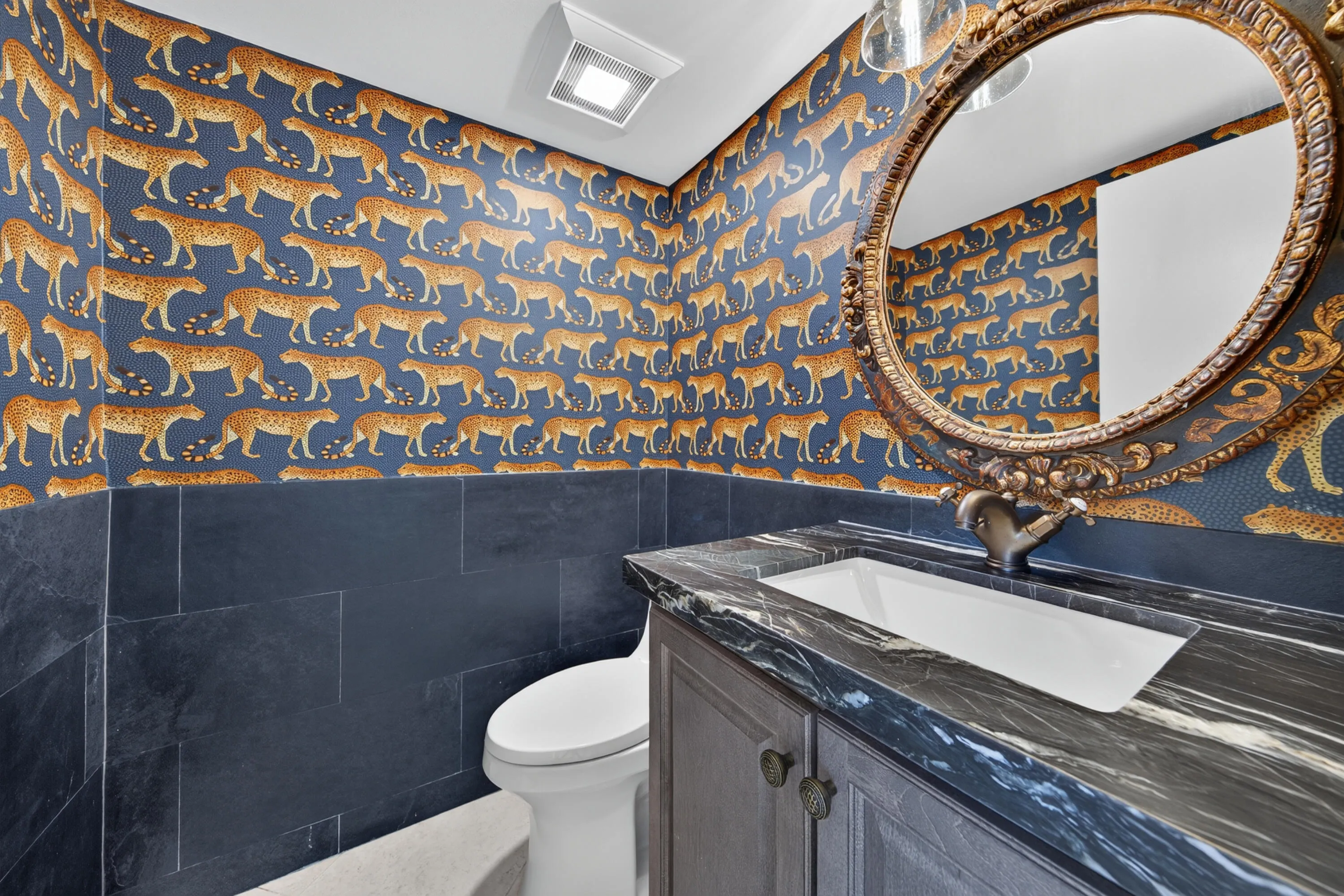 Distinctive powder room featuring dramatic designer wallcovering, stone surfaces and an elegant statement mirror.
