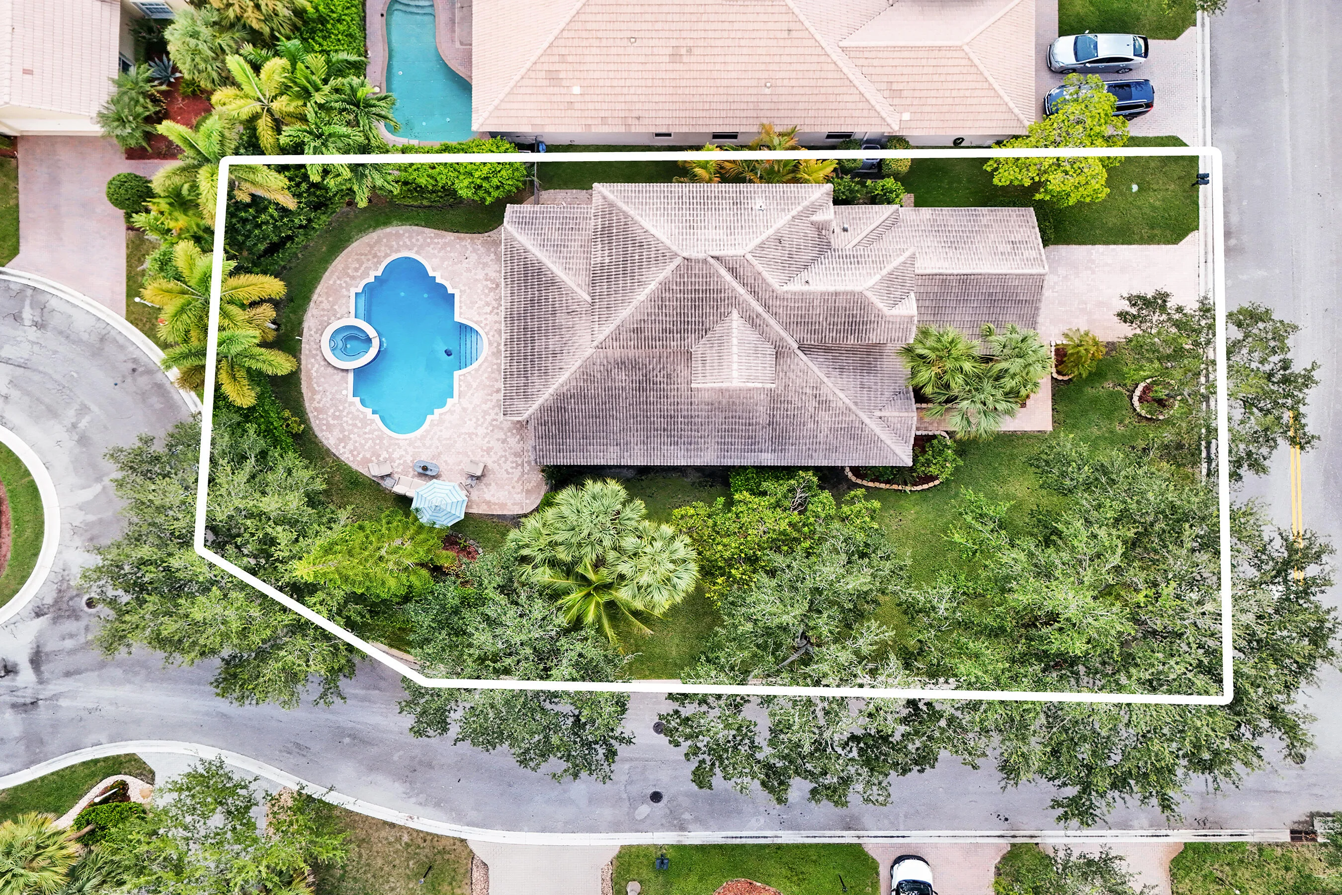 Curvilinear swimming pool with integrated spa, extensive paver patio, lush perimeter landscaping, and mature trees