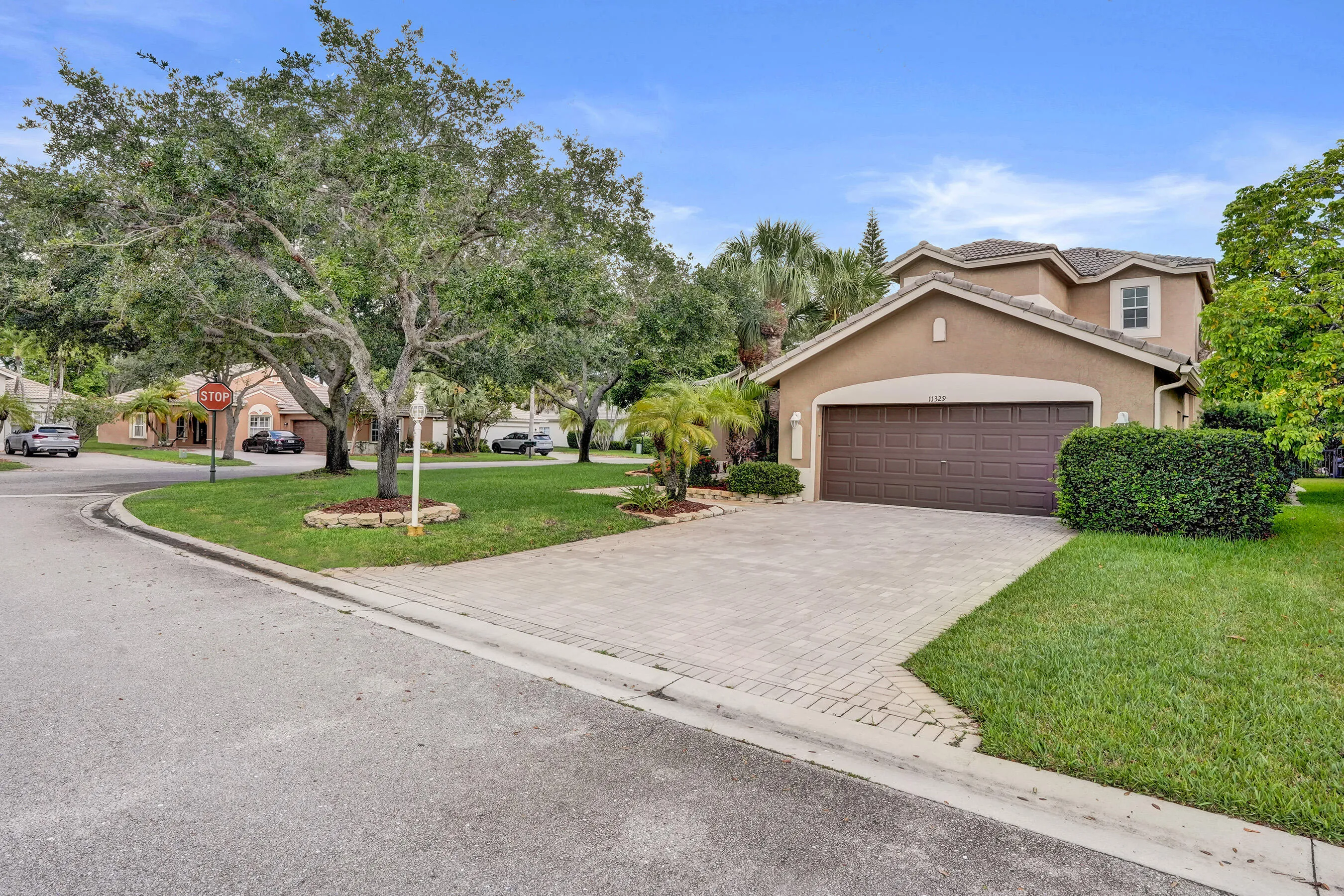 Stucco exterior with a tiled roof, two-car garage, paver driveway, and tropical landscaping