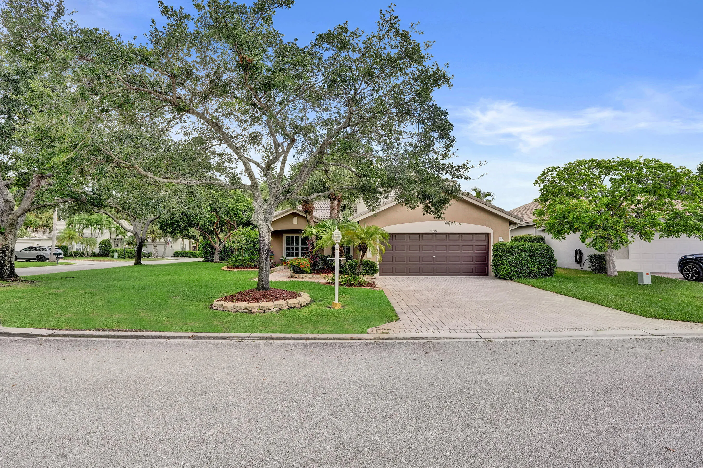 Two story residence featuring a two-car garage, an interlocking paver driveway, and a manicured lawn with mature trees