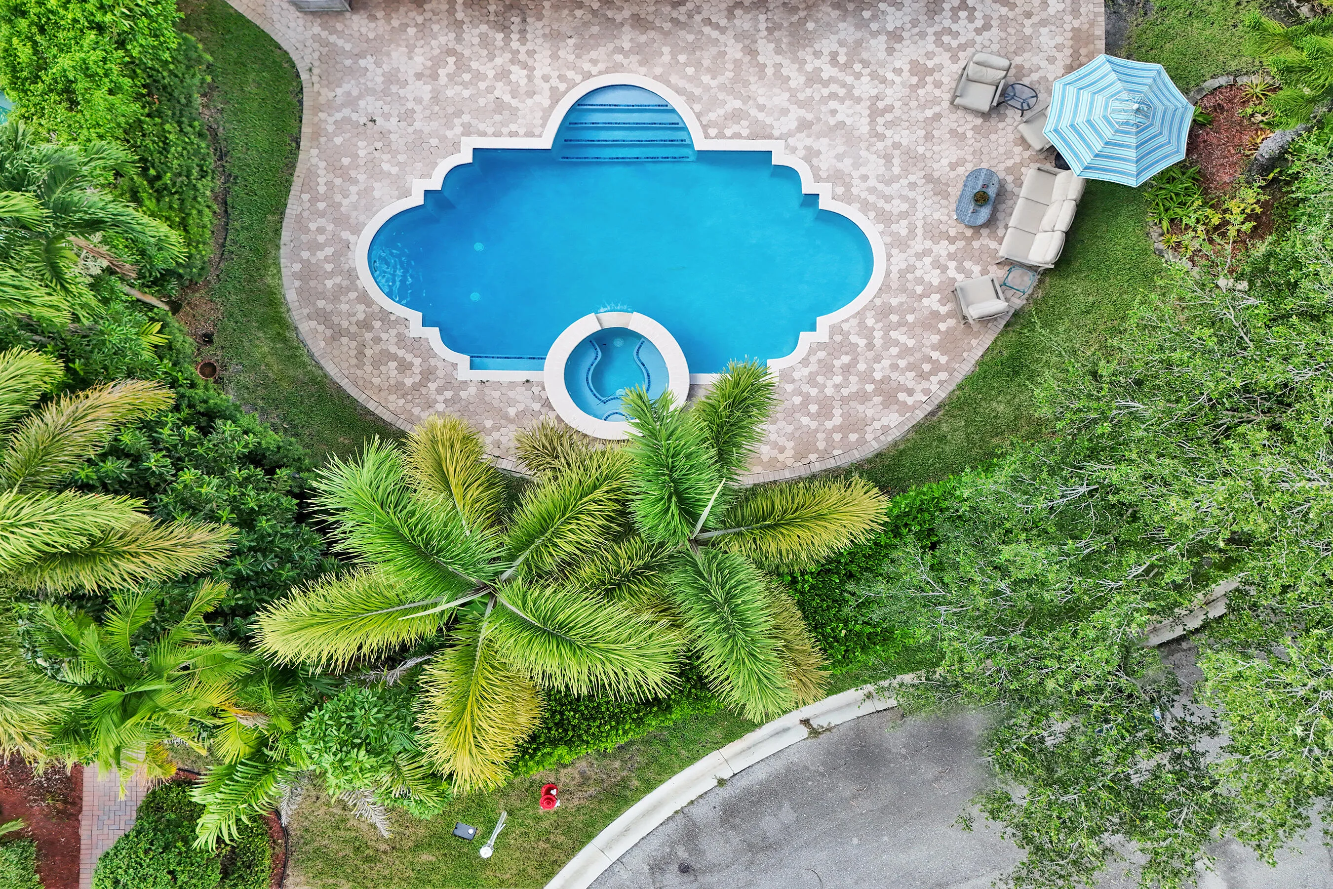 Custom-shaped swimming pool with an integrated spa, surrounded by a paver patio and lush landscaping