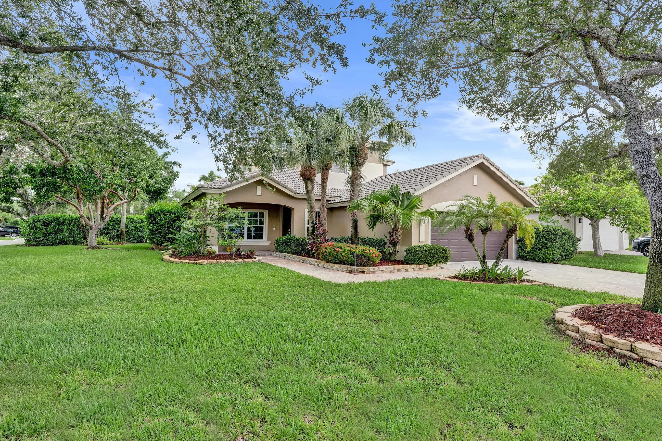Stucco exterior with a tiled roof, paver driveway, and mature landscaping