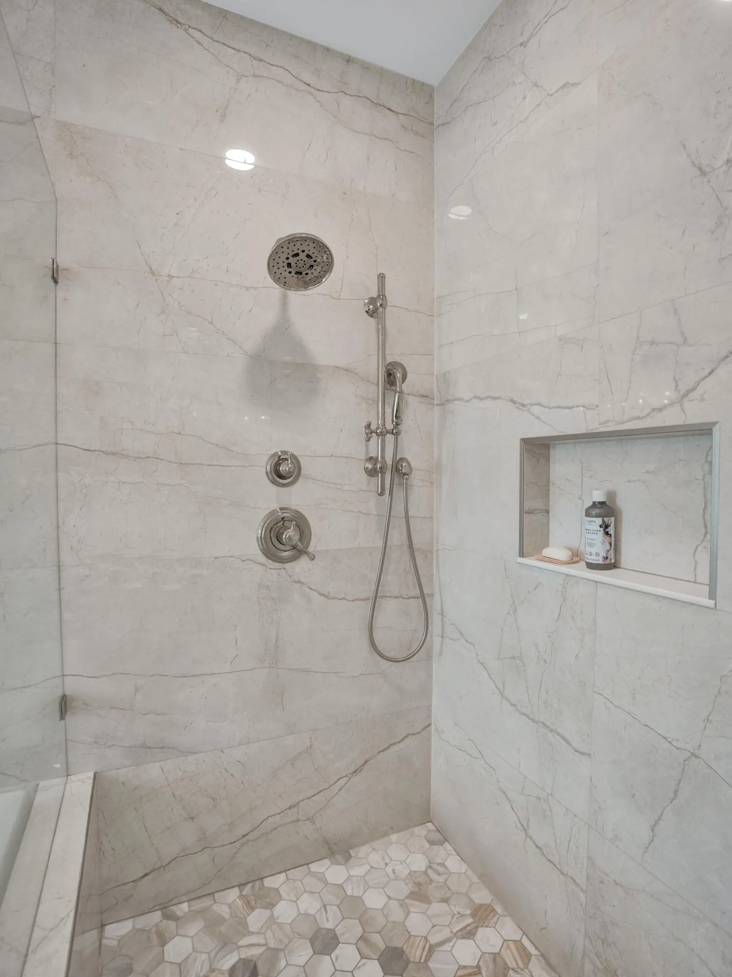 Shower featuring large format wall tiles, a rainfall showerhead, a handheld shower fixture, a recessed shower niche, and a hexagonal floor tile pattern