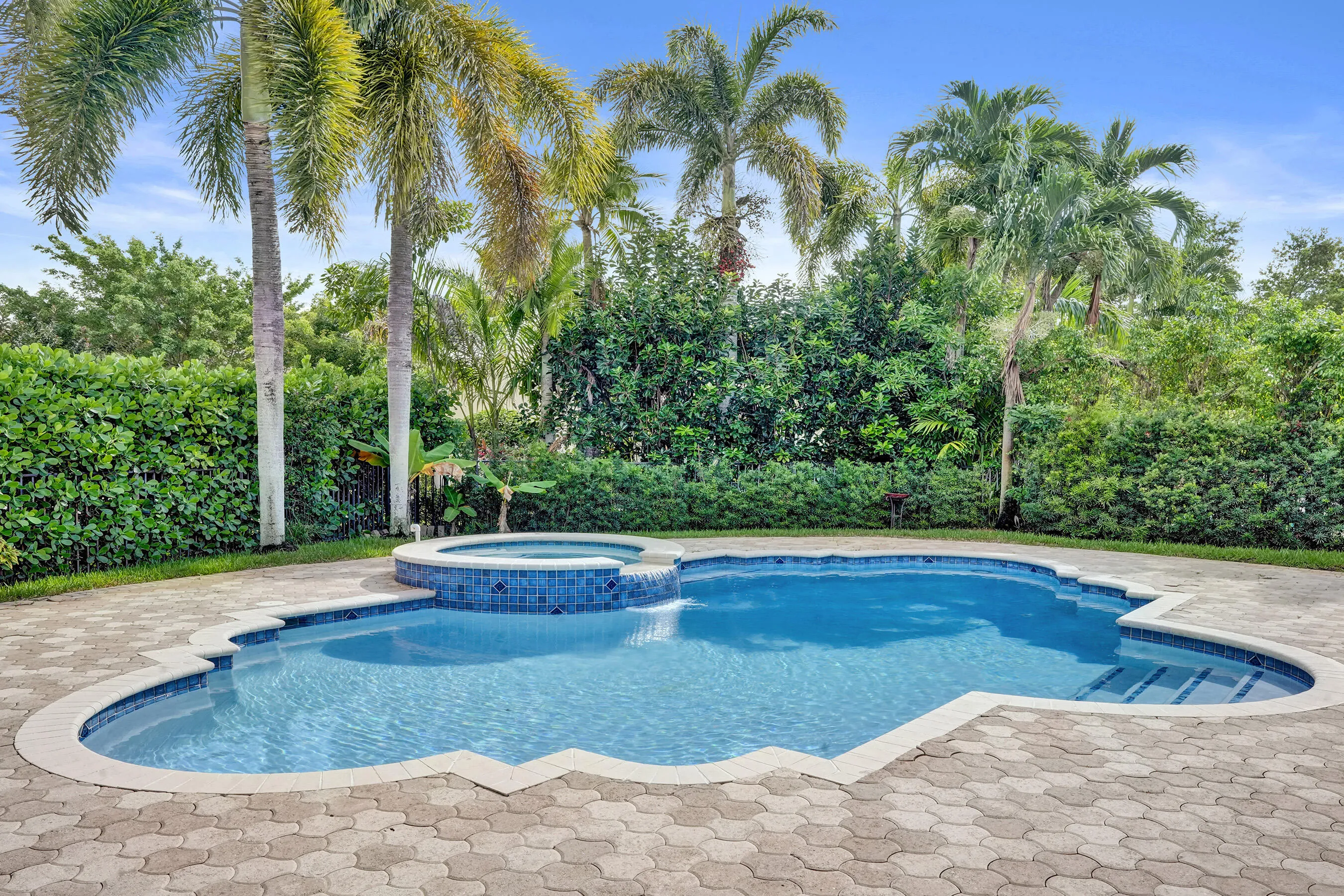 Swimming pool with blue mosaic tile, stone paver patio, and lush privacy hedge