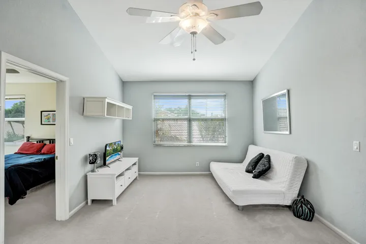 Vaulted ceiling with a ceiling fan, window with horizontal blinds, neutral wall paint, and light-colored carpet