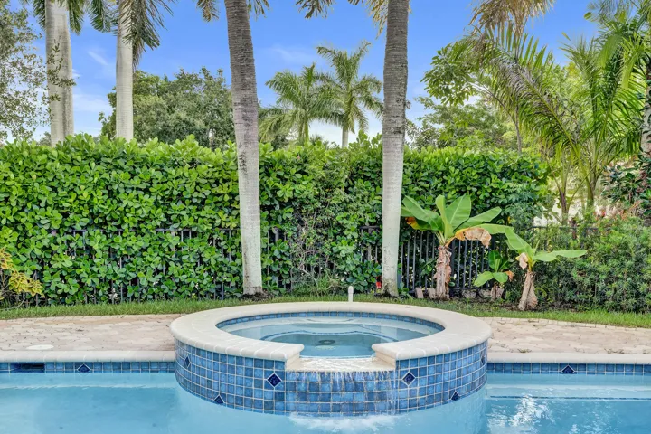 Integrated circular hot tub with blue mosaic tile detailing, stone coping, and a water feature