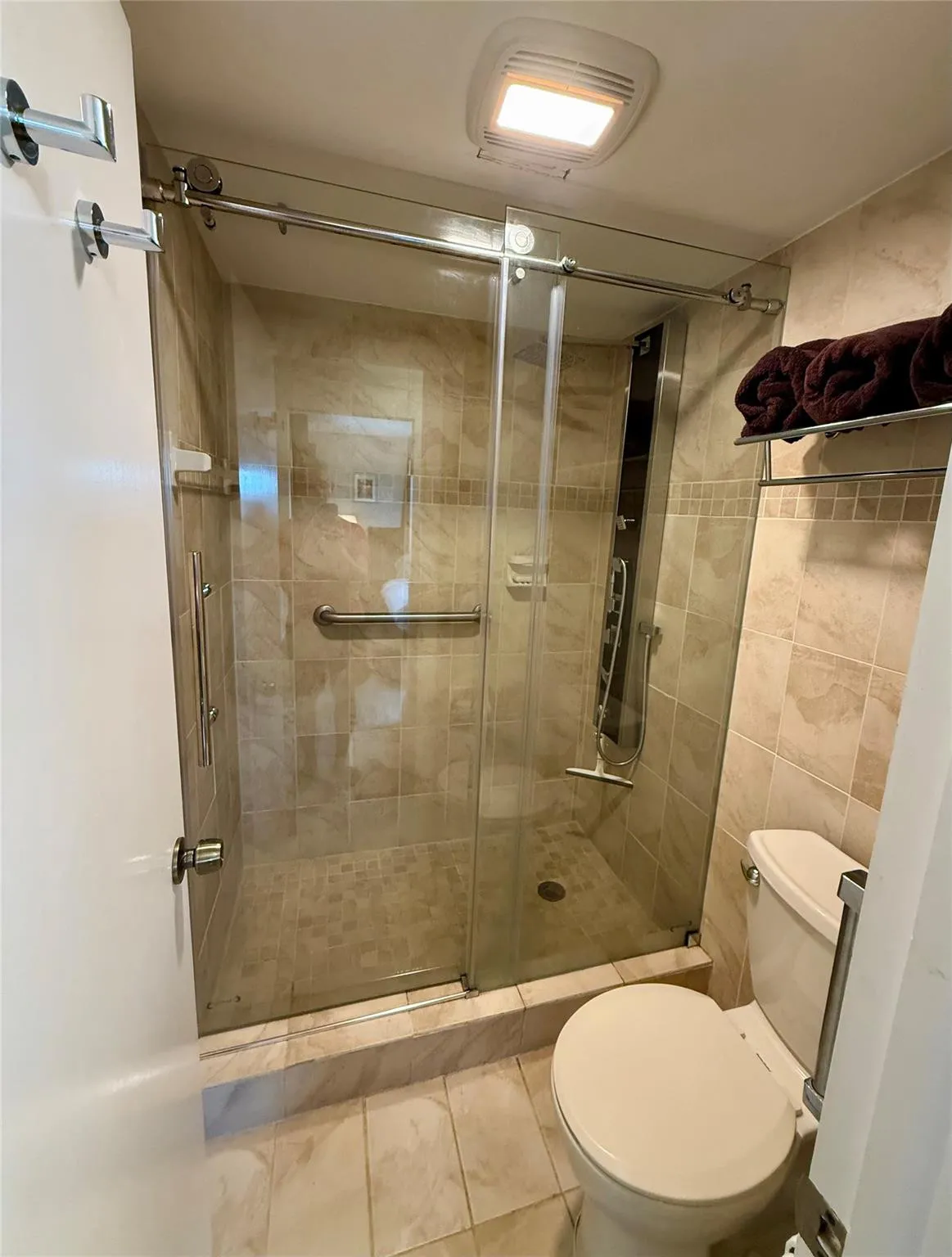 Tiled shower enclosure with sliding glass door, mosaic tile shower floor, and integrated grab bar