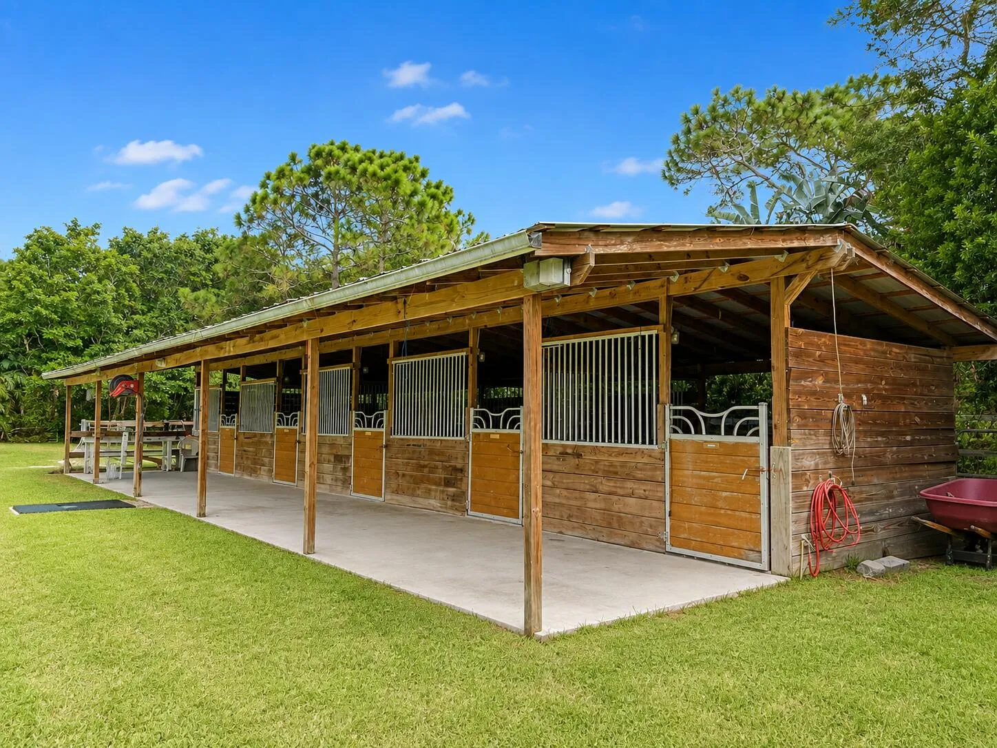 Wood-sided barn structure with multiple stalls, each featuring metal grating and wood doors