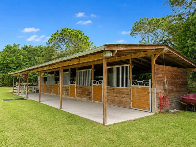 Wood-sided barn structure with multiple stalls, each featuring metal grating and wood doors