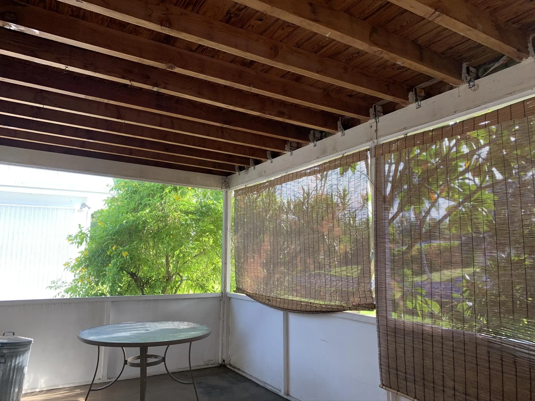 Covered outdoor patio with exposed wood ceiling beams and woven roll-up shades