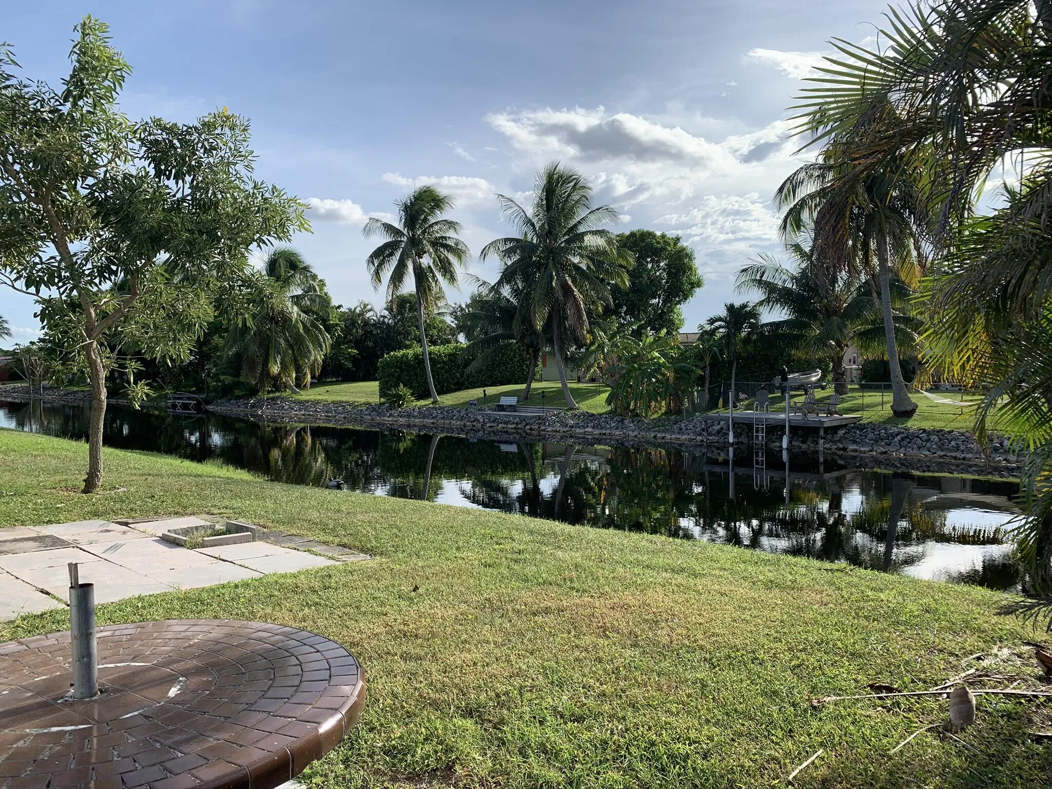 Canal frontage with a wooden dock structure, lush landscaping, and mature palm trees