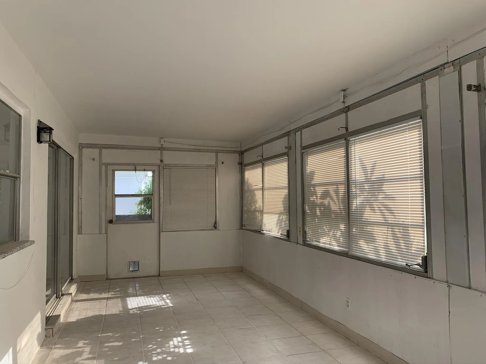Enclosed patio area featuring large windows with blinds, sliding glass door access, tiled flooring, and a ceiling-mounted light fixture