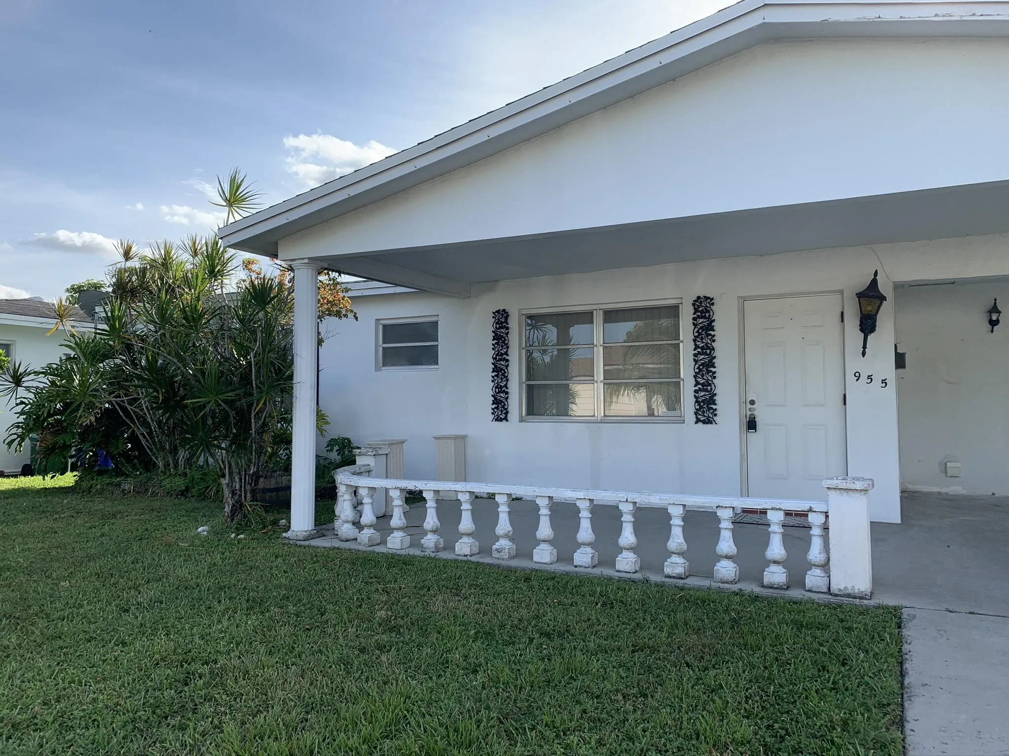 White exterior with a covered porch, decorative porch railing, and an exterior wall light fixture