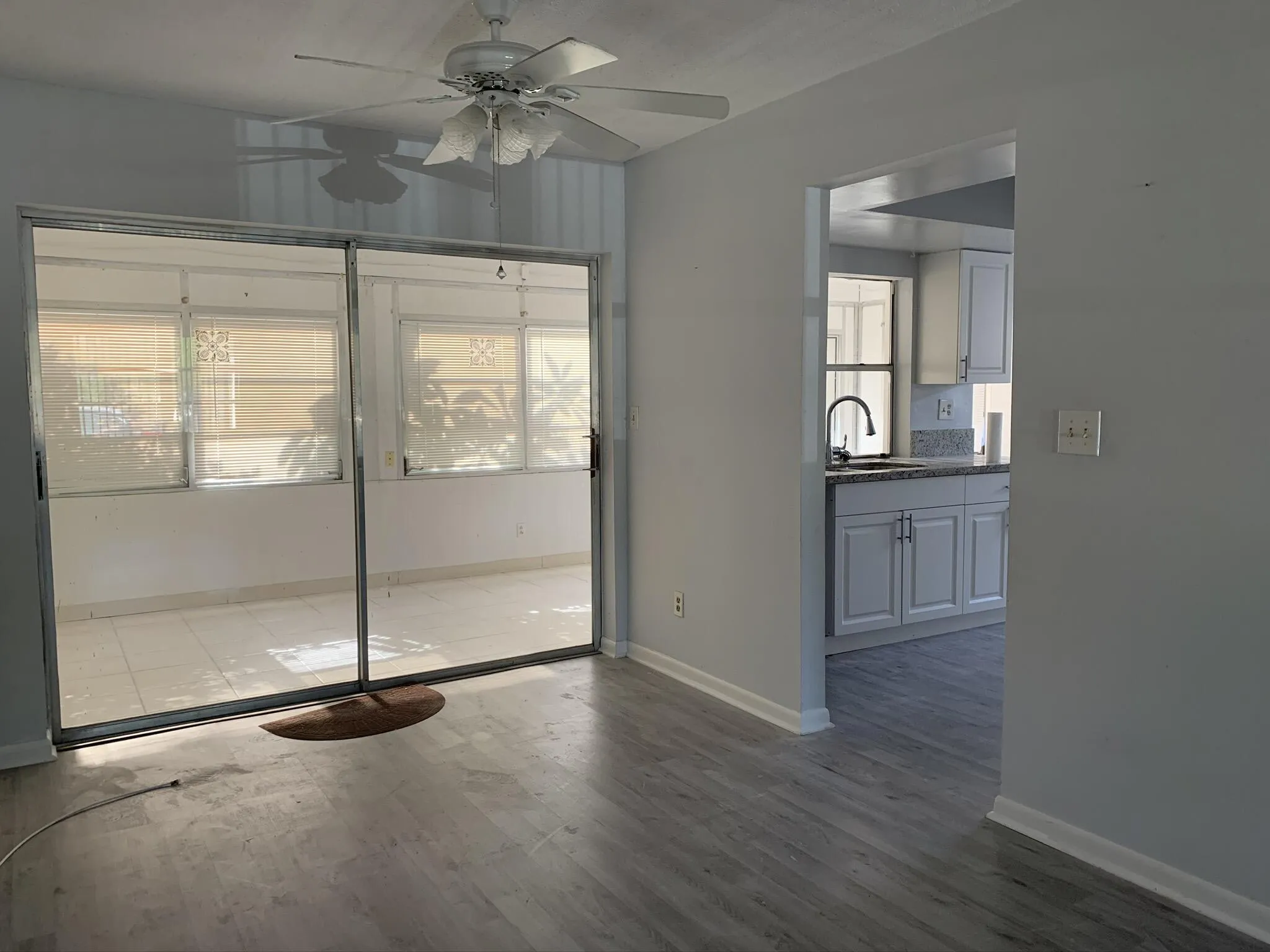 Wood-finish flooring throughout, bright interior with a ceiling fan, and sliding glass doors opening to a tiled enclosed patio