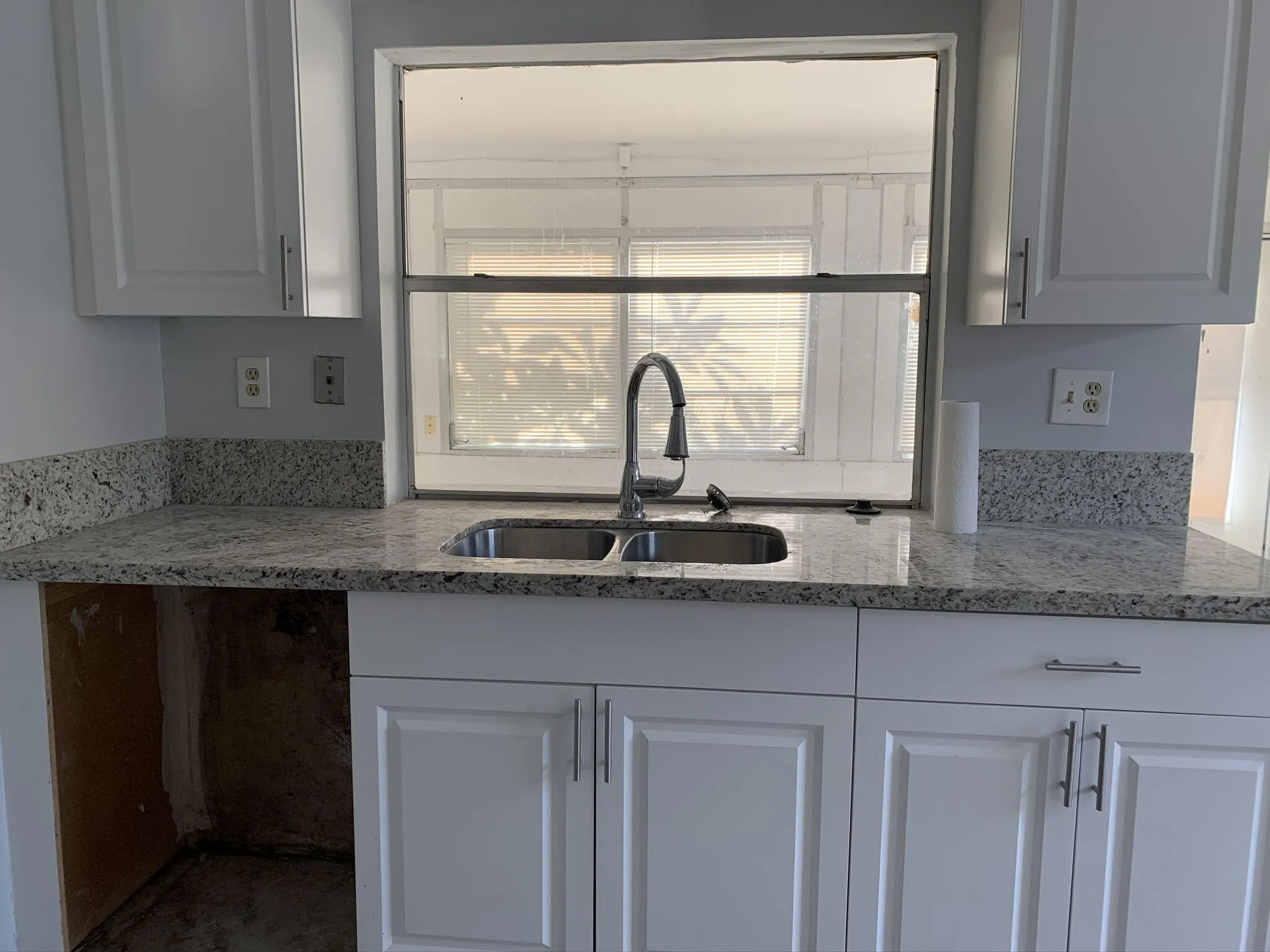White shaker-style cabinetry, patterned stone countertops with matching backsplash, stainless steel double basin sink, and a modern gooseneck faucet
