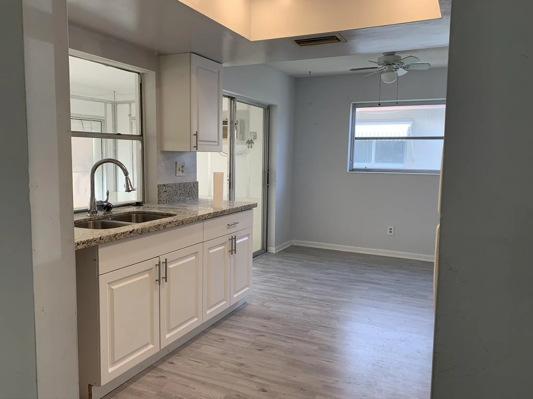 White cabinetry with brushed nickel hardware, light-toned granite countertop, stainless steel double basin sink with a high-arch faucet, and wood-finish flooring