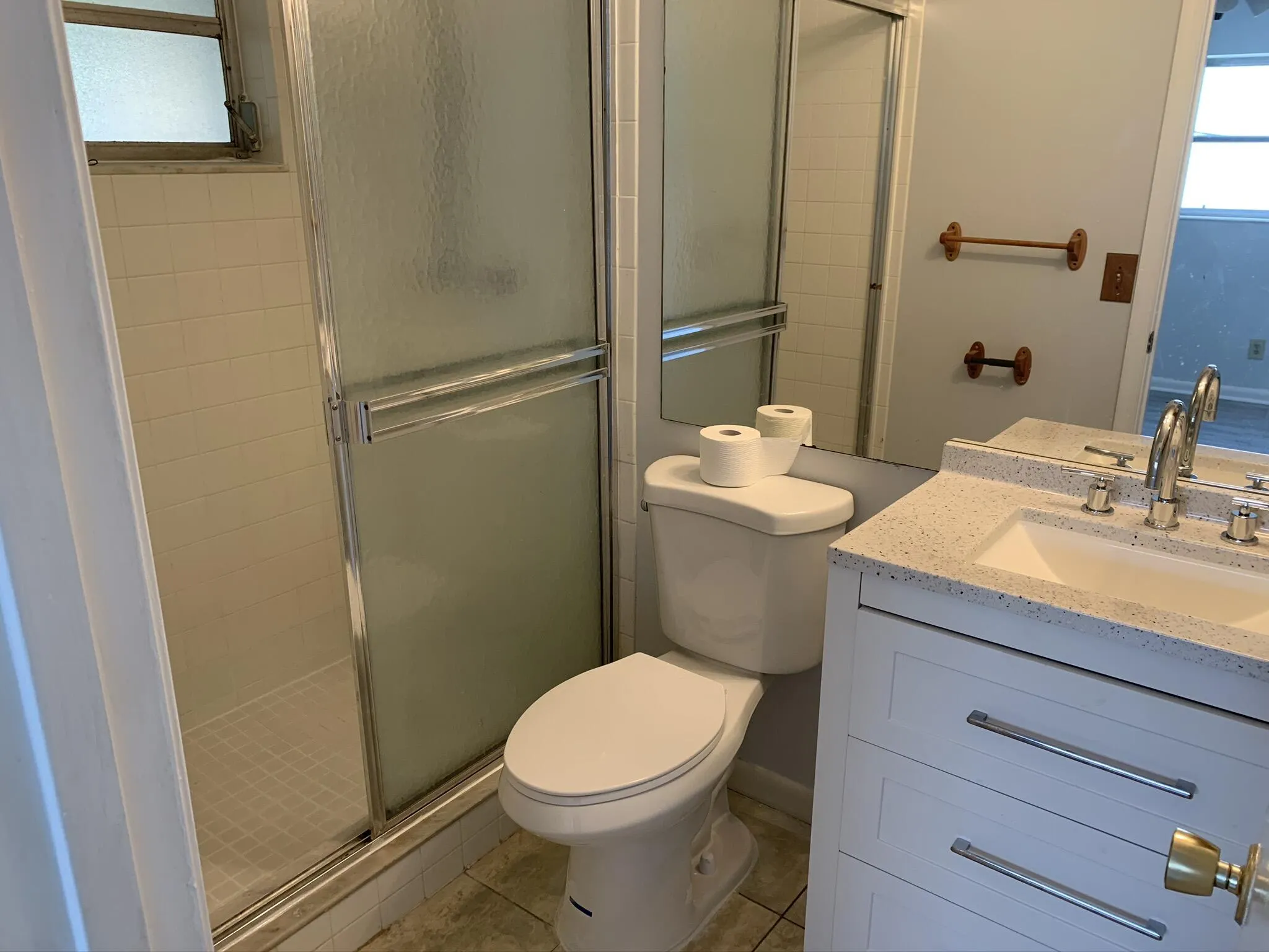 Tiled shower enclosure with sliding glass door, white vanity cabinet with chrome hardware, integrated sink, and a speckled countertop