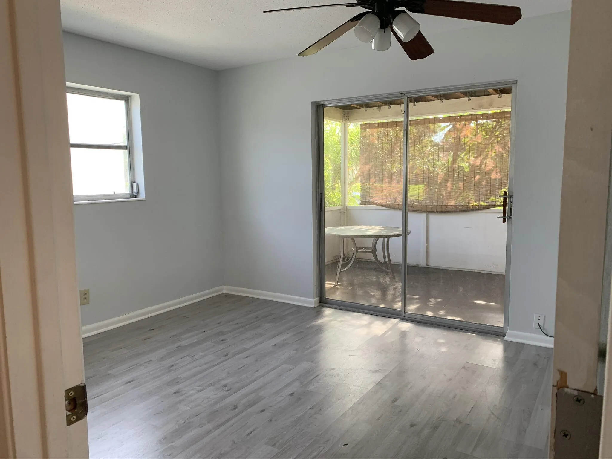 Wood-finish flooring, ceiling fan, and sliding glass door leading to a screened-in porch