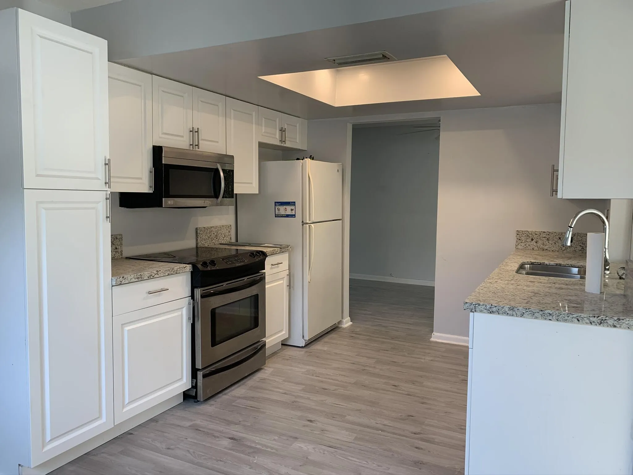 White cabinetry with brushed nickel hardware, stainless steel appliances, speckled stone-finish countertops, undermount sink with high-arc faucet, and wood-finish flooring