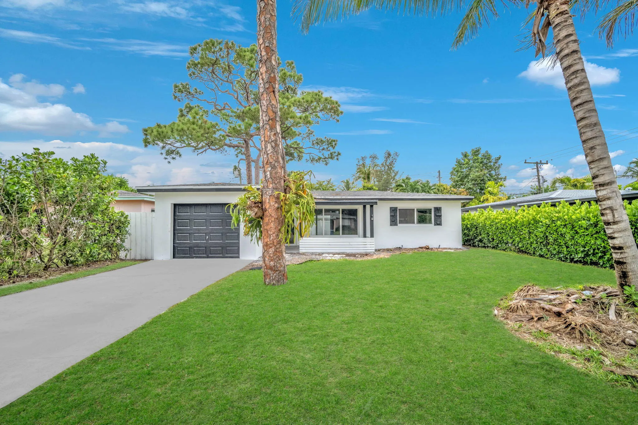 White exterior with a dark garage door, featuring a concrete driveway and an expansive front lawn