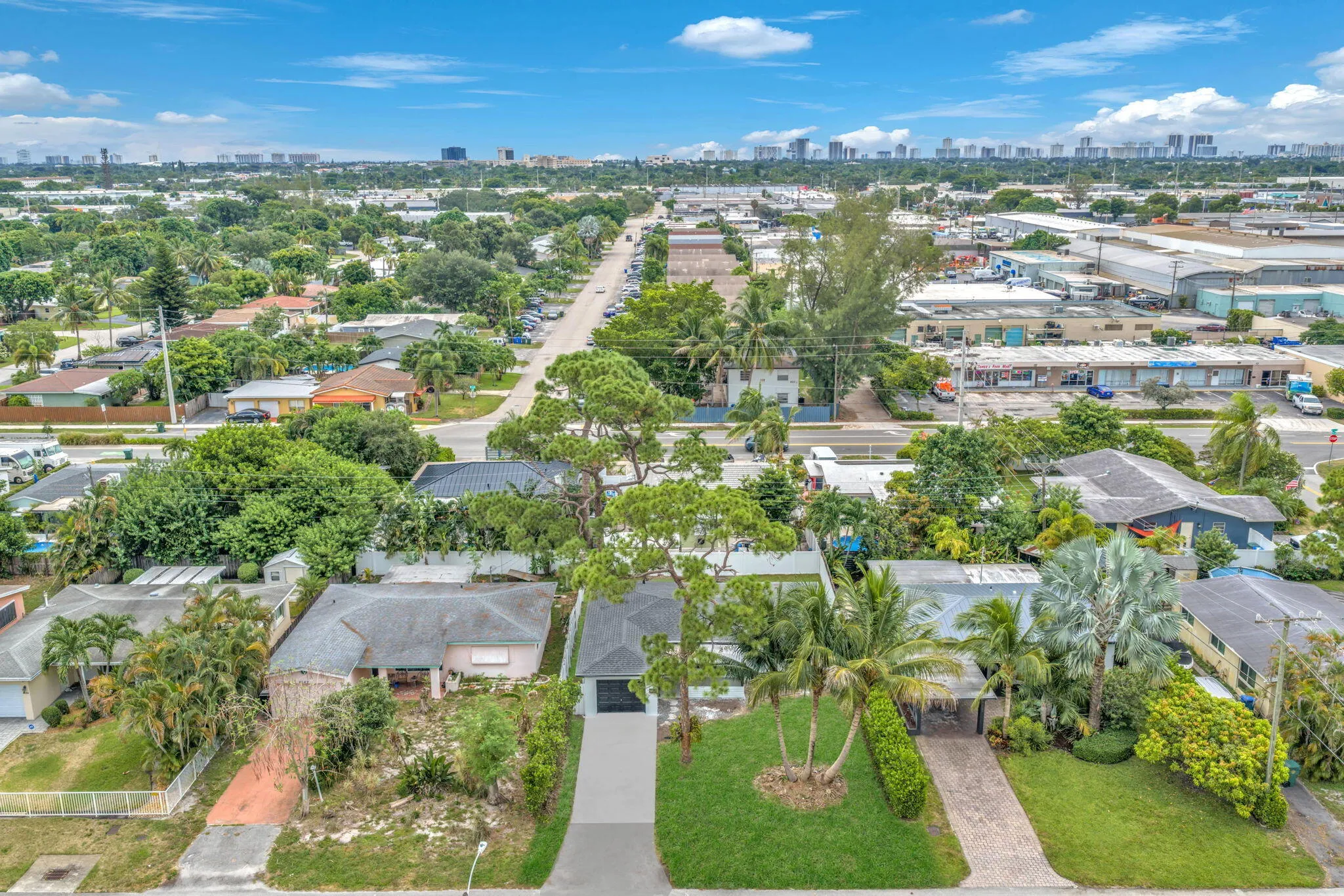 Aerial perspective showcasing a residential property with a paved driveway, surrounded by lush landscaping and mature trees
