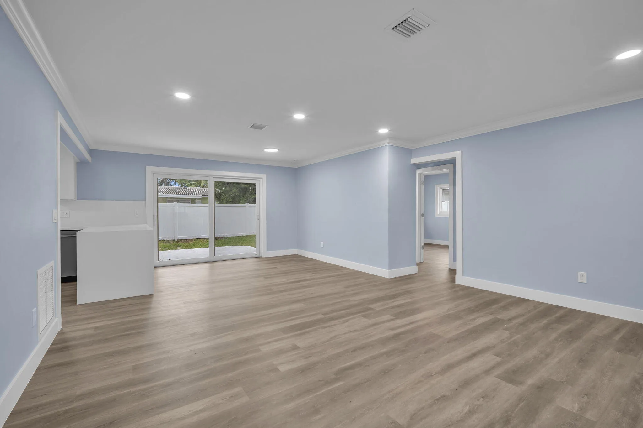 Wood-finish flooring throughout, recessed lighting, crown molding, and sliding glass doors leading to a patio