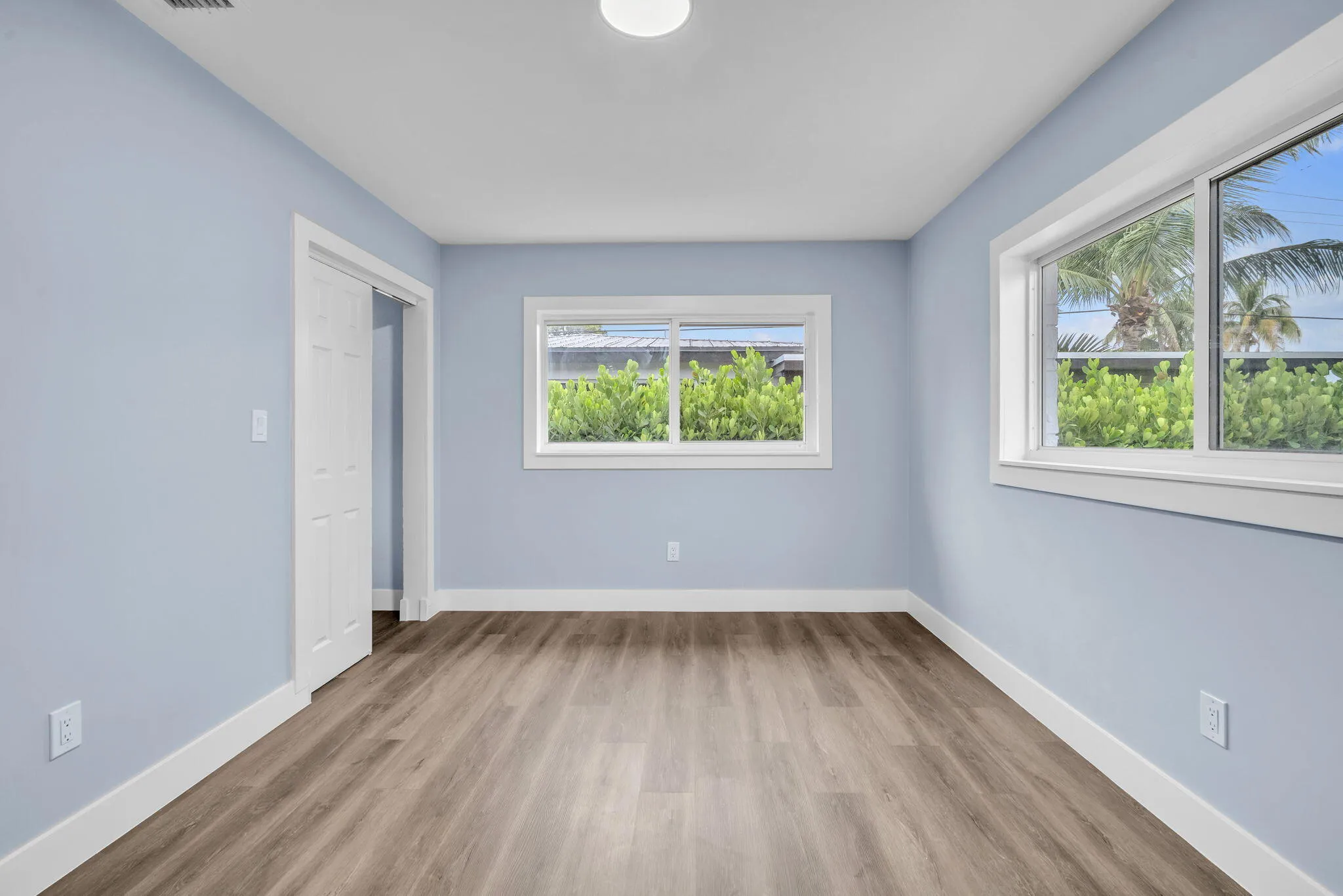 Wood-finish flooring, white trim, sliding closet door, and multiple windows