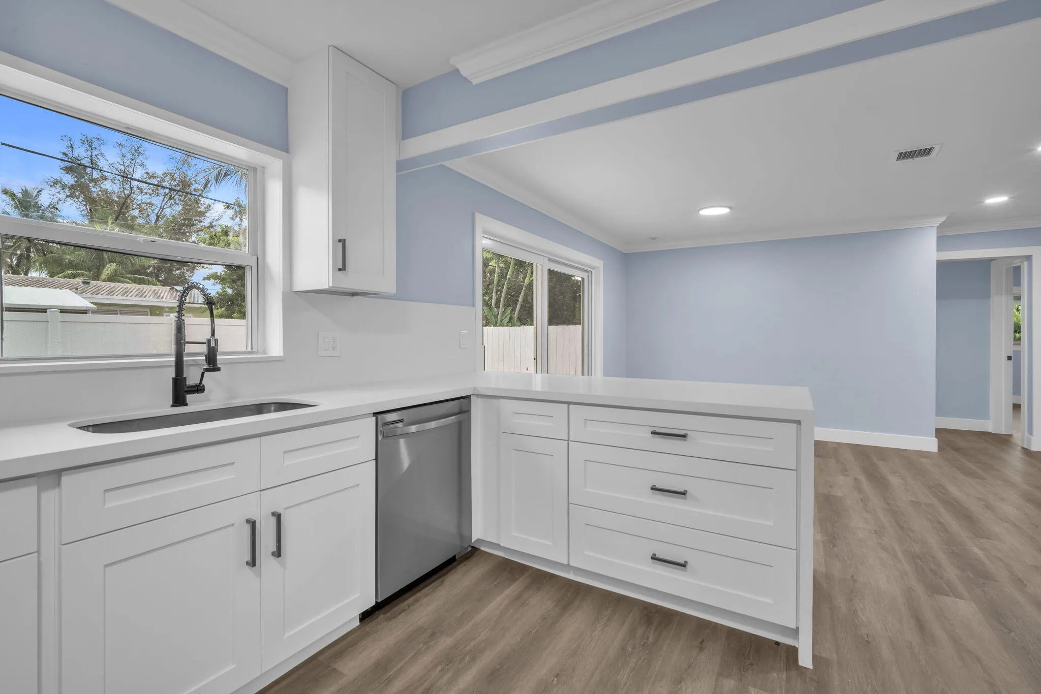 White shaker cabinetry with modern black hardware, stainless steel dishwasher, undermount sink with a matte black faucet, light-toned wood-finish flooring, and white countertops