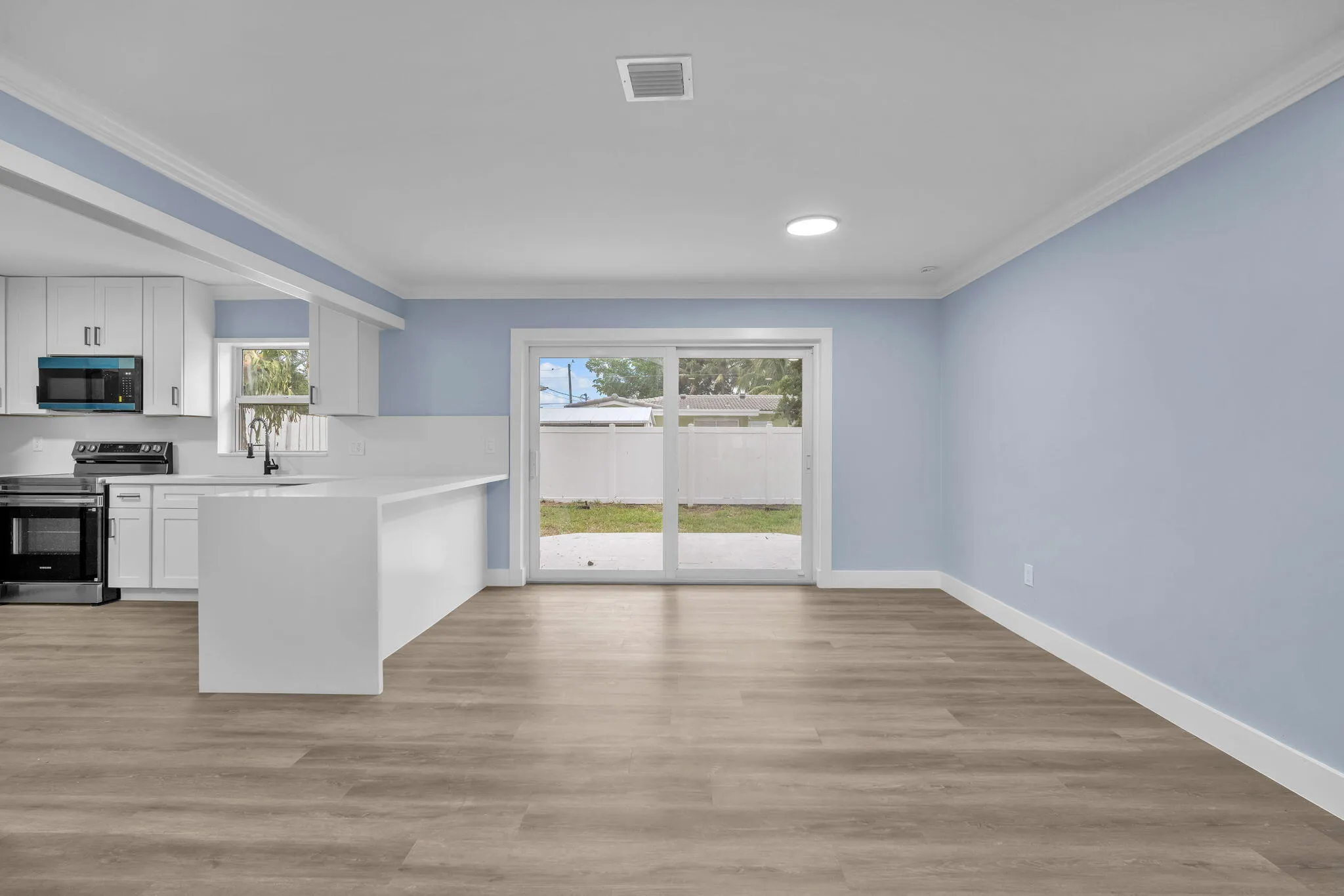Open-concept living space featuring wood-finish flooring, a kitchen island with seating, white cabinetry, stainless steel appliances, and a sliding glass door to the exterior