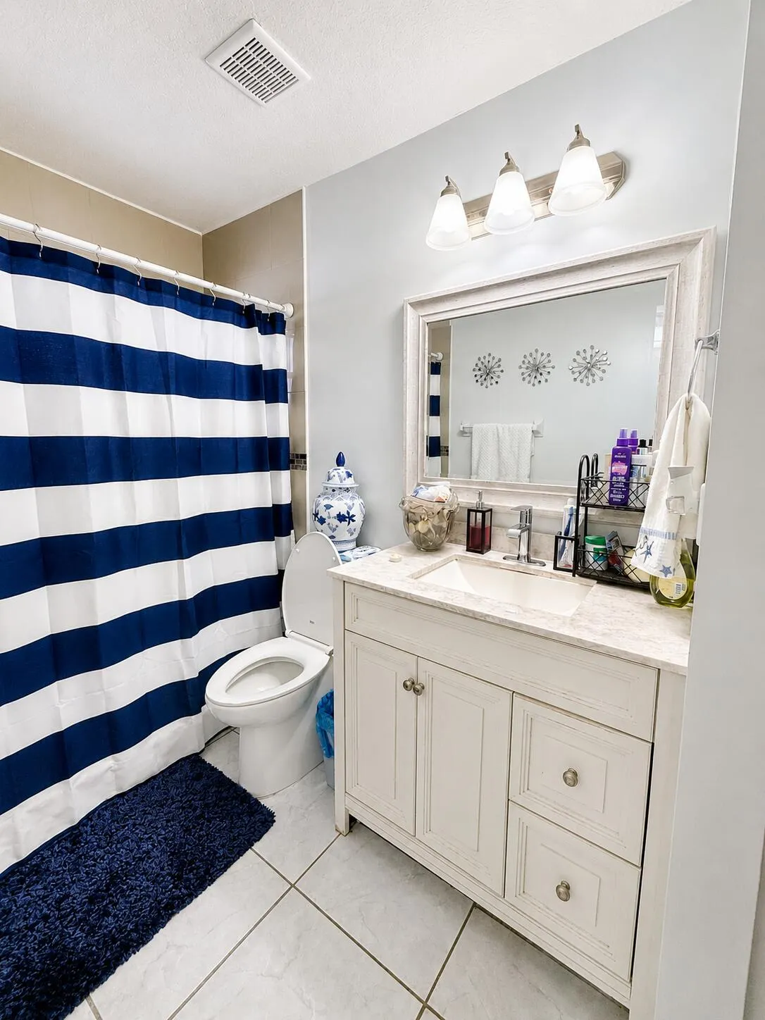 White vanity with dual cabinet doors and two drawers, integrated sink with chrome faucet, a large framed mirror, and a three-light fixture
