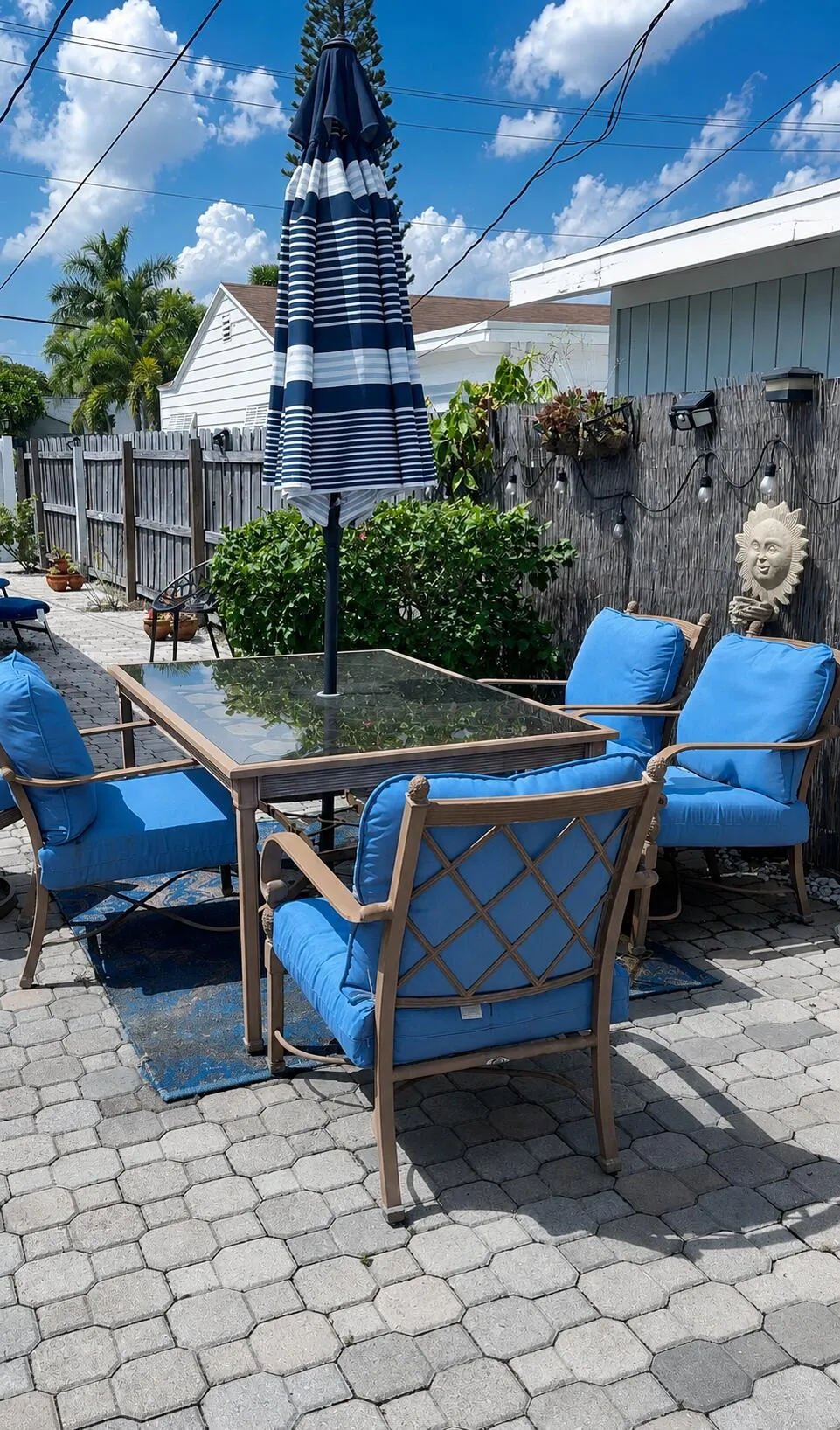 Paver patio featuring a wooden privacy fence, established shrubbery, and exterior string lighting
