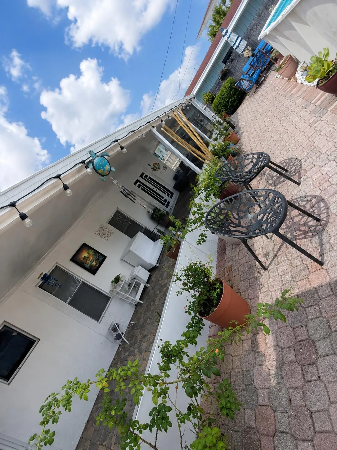 Paved patio area, string lighting, white exterior, multiple windows, and potted plantings