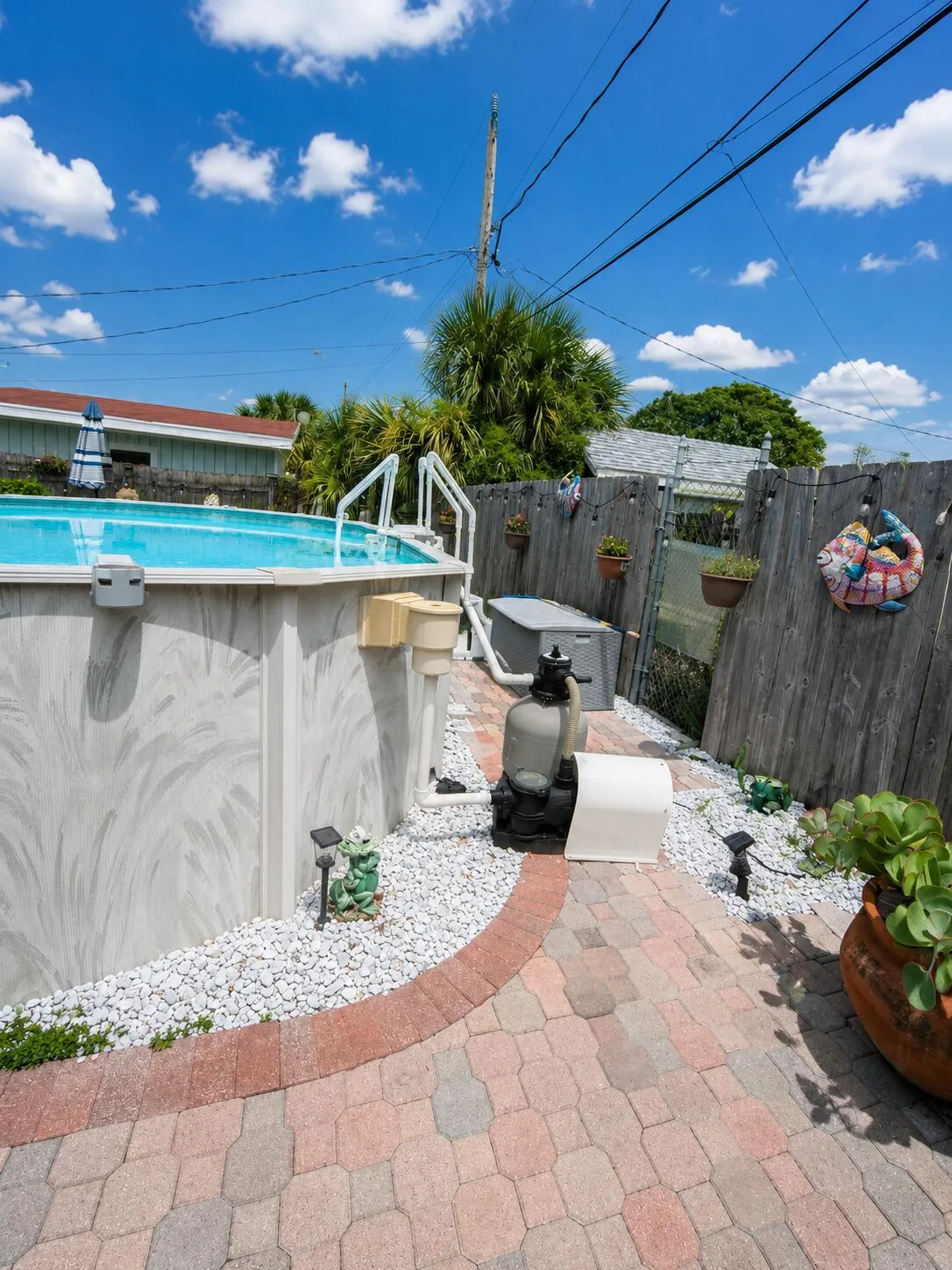 Above-ground pool with white steps, surrounded by a paver patio and white stone landscaping